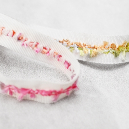 Ozdobna taśma rypsowa w kolorze off-white, wykończona kolorowymi nitkami.